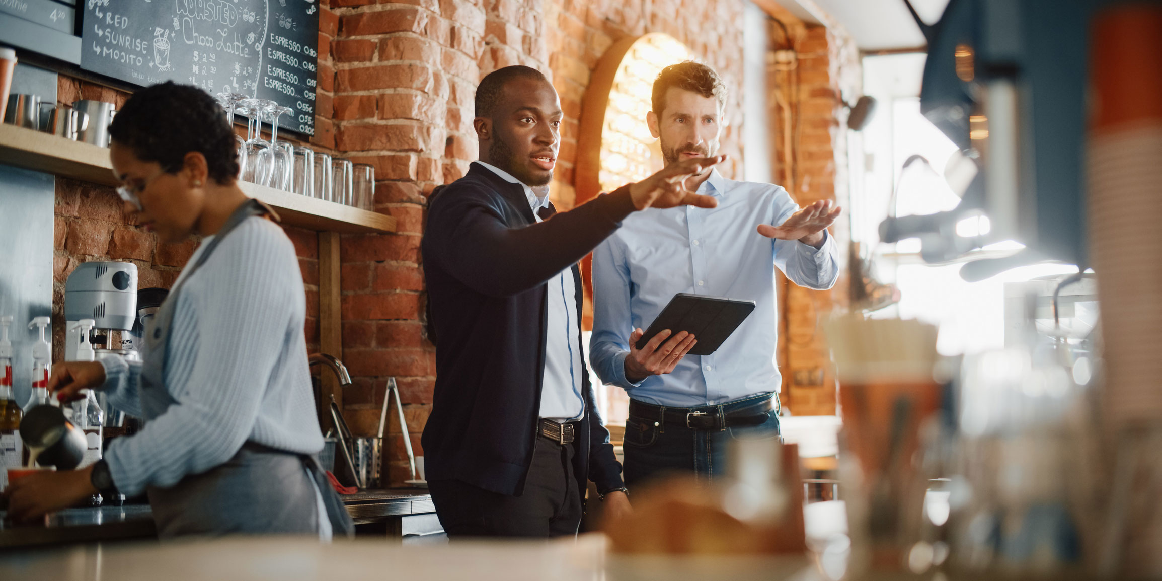 Barista making coffee while two gentlemen converse